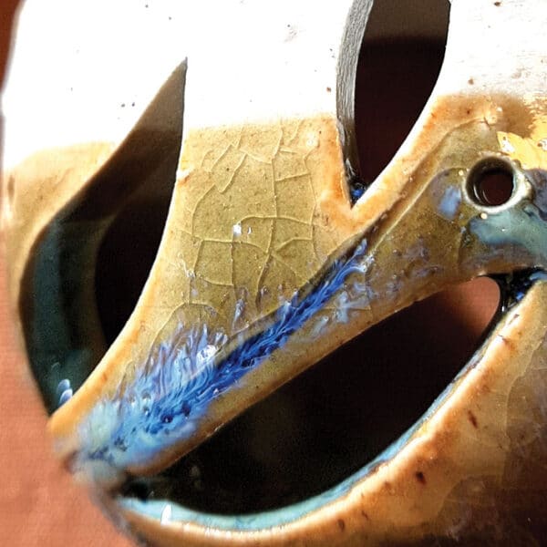 Détail. Brule-résine en terre de grés, émaillé bicolore, transparent et bleu-vert, décor de flamme. A l'intérieur se trouve une bougie chauffe-plat et au dessus, une grille permettant de déposer quelques grains de résines. Permet de parfumer un lieu, ou de le nettoyer des mauvaises énergies stagnantes.