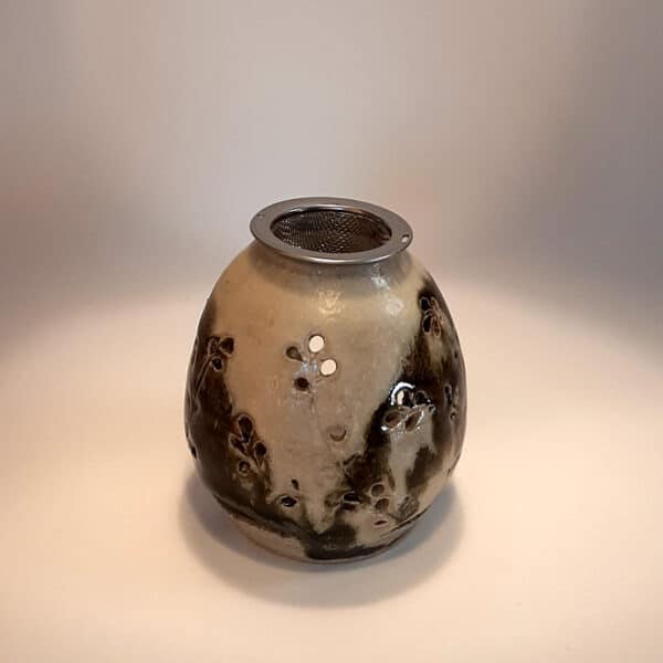Brule-résine en terre de grés, émaillé bicolore, noir et ivoire, décor de fleurs. A l'intérieur se trouve une bougie chauffe-plat et au dessus, une grille permettant de déposer quelques grains de résines. Permet de parfumer un lieu, ou de le nettoyer des mauvaises énergies stagnantes.