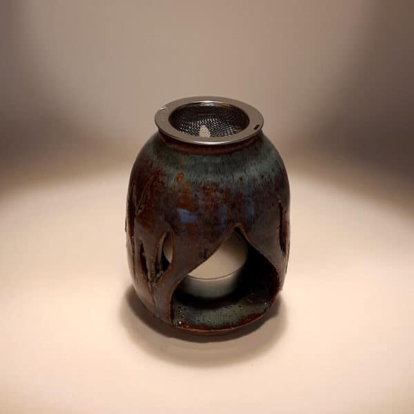 Brule-résine en terre de grés, émaillé marron/bleu, décor de feuille. A l'intérieur se trouve une bougie chauffe-plat et au dessus, une grille permettant de déposer quelques grains de résines. Permet de parfumer un lieu, ou de le nettoyer des mauvaises énergies stagnantes.