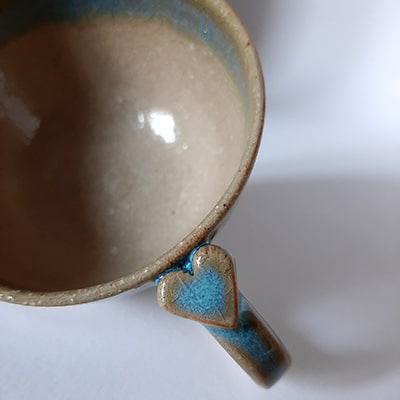 Tasse avec anse en grès émaillé, décorée sur la celle-ci d'un joli cœur. Forme ronde en 2 couleurs transparent et bleu. Tasse pour café.