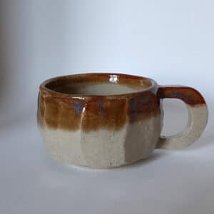 Vue de face. Tasse en grés émaillé transparent et liseré caramel au reflet bleu.