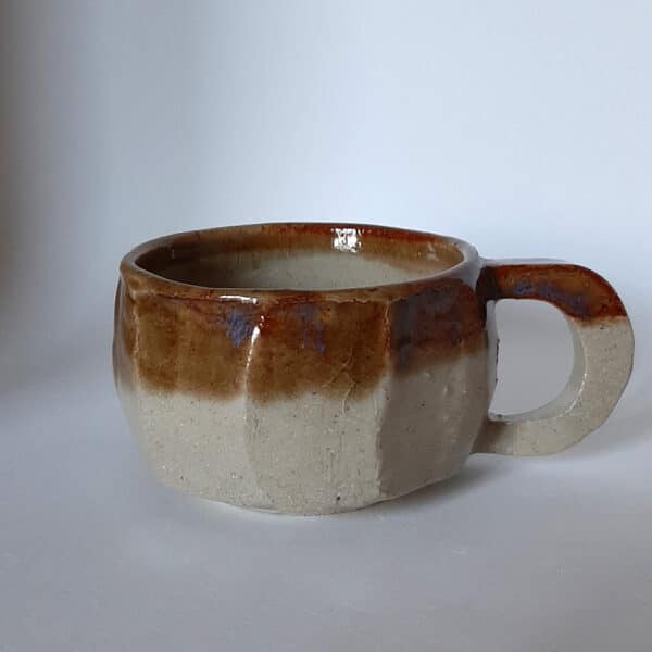 Vue de face. Tasse en grés émaillé transparent et liseré caramel au reflet bleu.