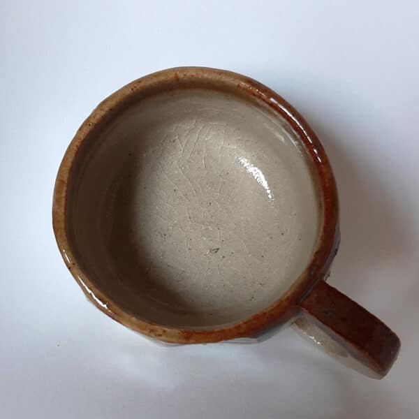 Vue de dessus. Tasse en grés émaillé transparent et liseré caramel au reflet bleu.