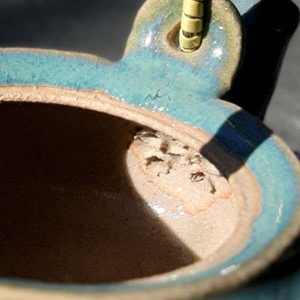 Théière en grés émaillé avec anse en osier et ruban synthétique. Collection Lagon, un émail transparent qui diffuse un ruban turquoise sur le bord de la pièce. Un détail du filtre incorporé ce qui permet de filtrer toute sorte de thé.