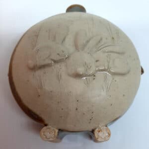 Dans la collection des "Elégantes", vase en grés émaillé Azurite avec motif de lapin sur face avant sur fond transparent. Céramique aux 2 couleurs bleu et marron sur l'arrière, au dos et côté avec effet de matière.